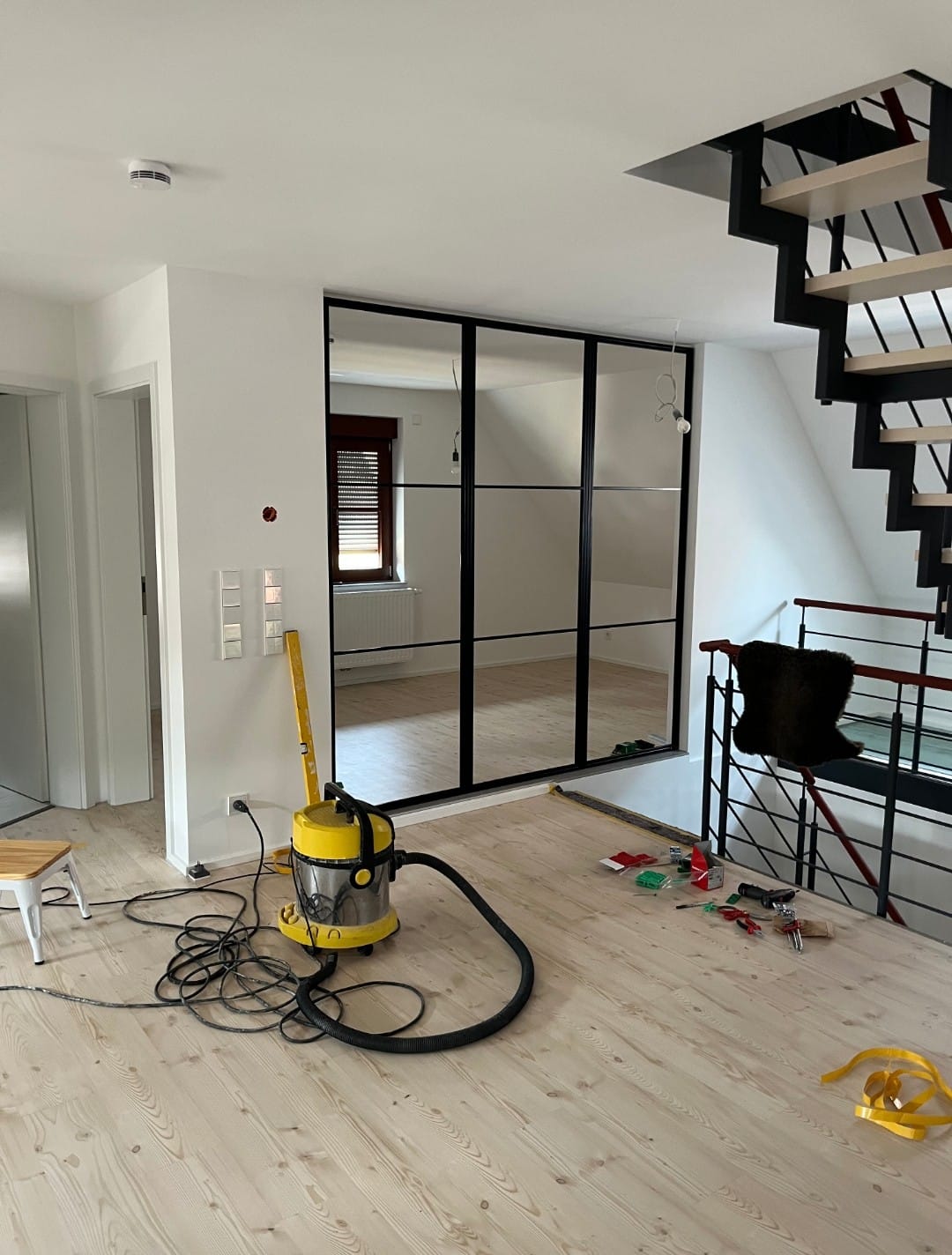 Wohnraumrenovierung in Stuttgart mit hellem Laminatboden, moderner Metalltreppe und maßgefertigtem Spiegel im Industriestil.